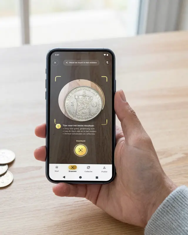 A hand holds a phone above the kitchen table, next to a jar of old coins. On screen, AI Coin Collector identifies a silver 1929 guilder: Wilhelmina 1 gulden, estimated value €18.